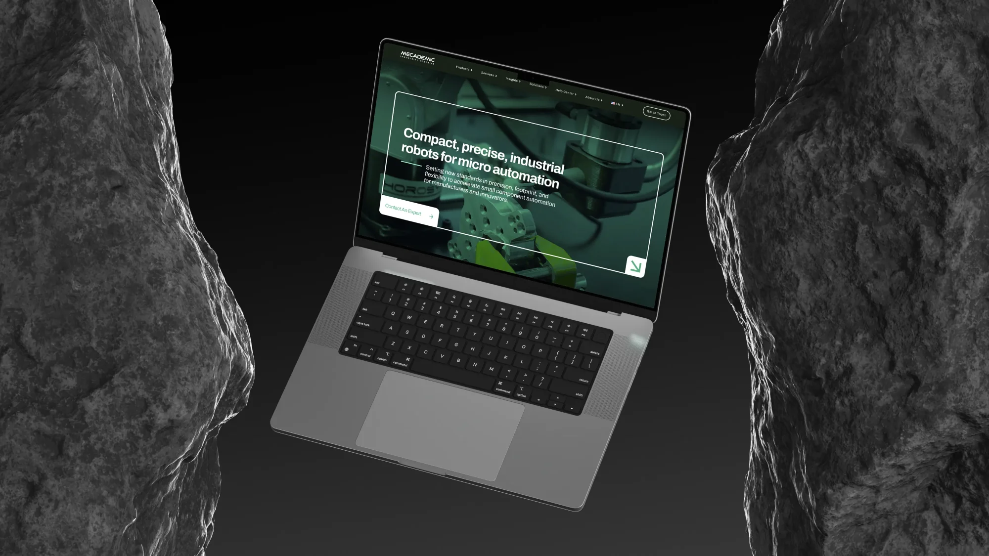 mecademic.com on a laptop, staged between two dark rock monoliths.