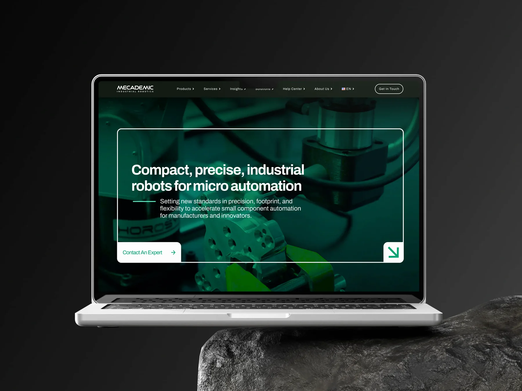 mecademic.com on a laptop, staged between two dark rock monoliths.