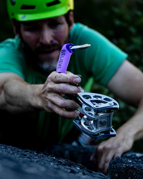 A climber clipping the purple BELIEVE sleeve to a cam.