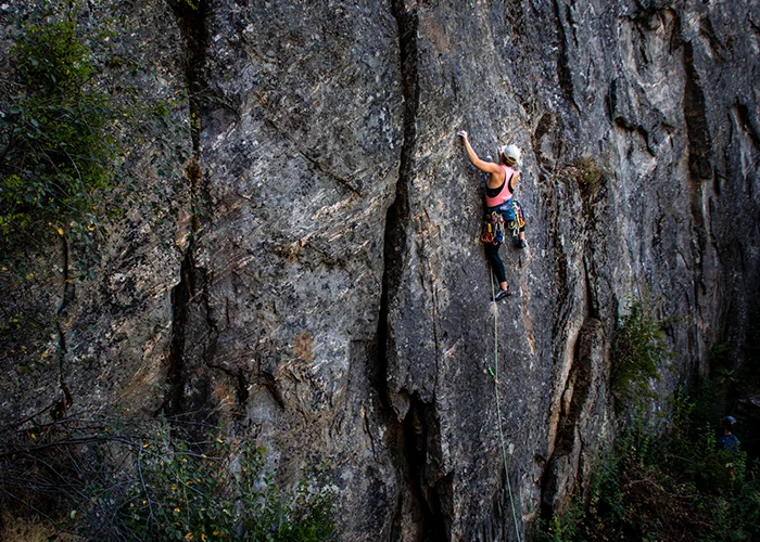 A climber high on a grey rock face, rope trailing below.